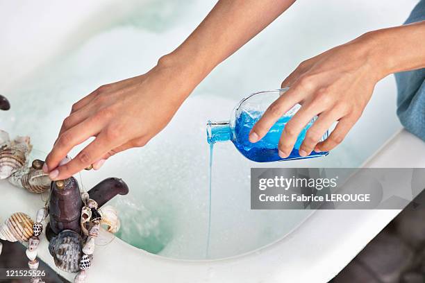 close-up of a woman's hand pouring aromatherapy oil in a bathtub - essence day stock pictures, royalty-free photos & images