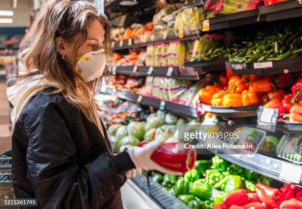 shopping during a pandemic. a young woman wearing protective mask and gloves shopping vegetable in a store. - epidemiology stock pictures, royalty-free photos & images