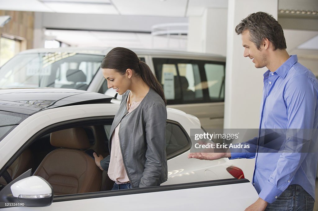 Young woman checking car from inside while man holding the door