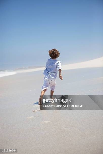 rear view of a boy running on beach - boy barefoot rear view stock-fotos und bilder