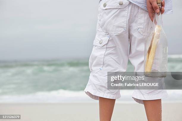 close-up of boy holding bottle with message on the beach - message in a bottle stock pictures, royalty-free photos & images