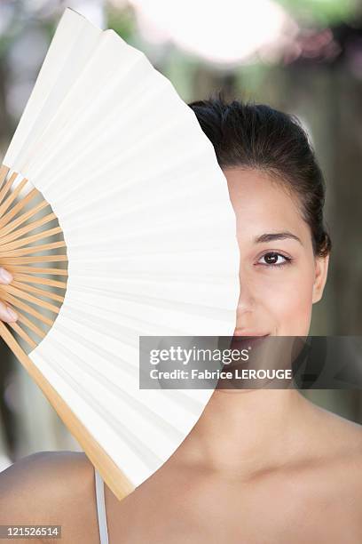 beautiful young woman holding a chinese fan in front of her face - waaier stockfoto's en -beelden