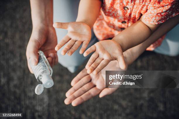 mother squeezing hand sanitizer onto little daughter's hand outdoors to prevent the spread of viruses during the covid-19 health crisis - händedesinfektion stock-fotos und bilder