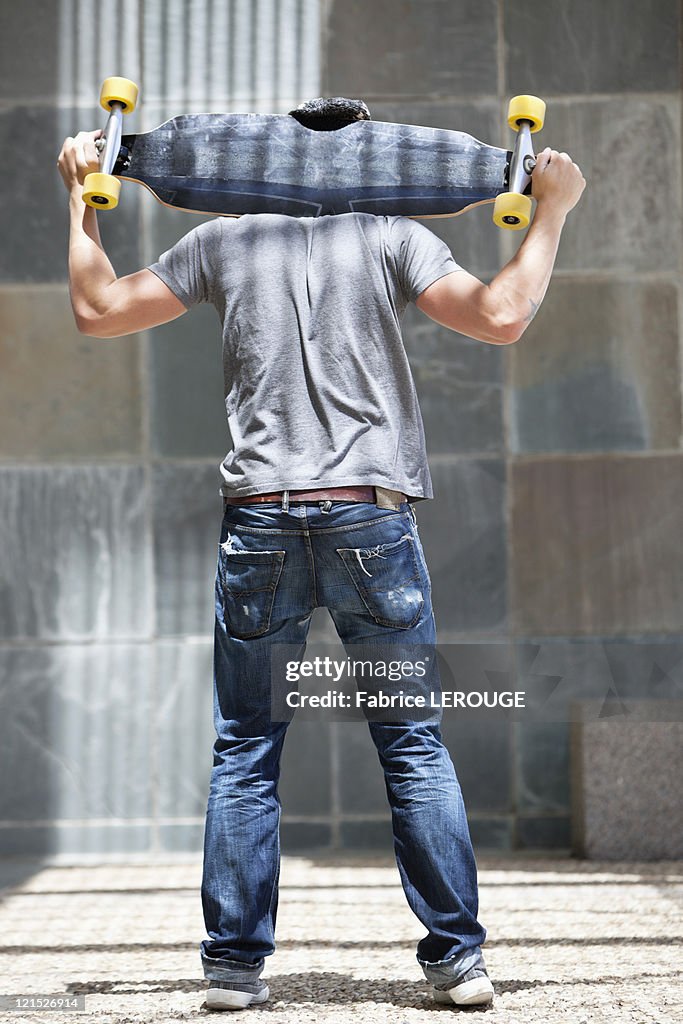 Rear view of man holding skateboard on shoulders