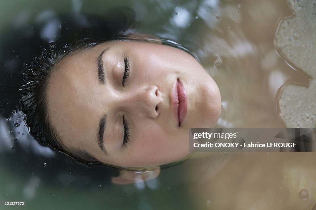 Beautiful young woman relaxing in a bathtub with her eyes closed