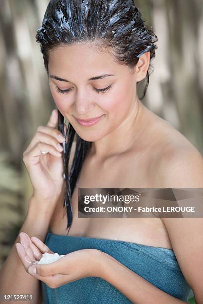 beautiful young woman wrapped in towel and applying deep conditioner - conditioner imagens e fotografias de stock