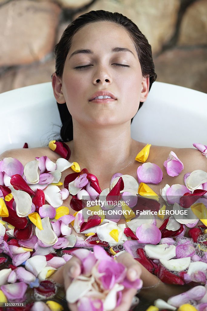 Beautiful young woman relaxing in bathtub with petals