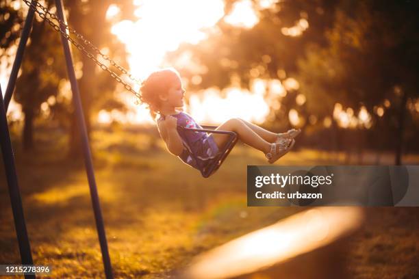 kleines mädchen schwingt bei sonnenuntergang - schaukel stock-fotos und bilder