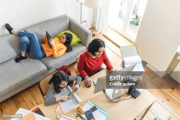 donna con due figlie che lavorano in ufficio a casa in soggiorno - tecnologia mobile foto e immagini stock