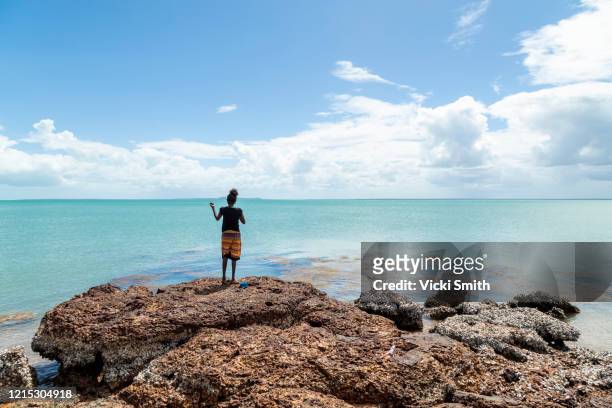 young indigenous woman standing on rocks fishing into the waters of the vast ocean - fishing australia stock pictures, royalty-free photos & images