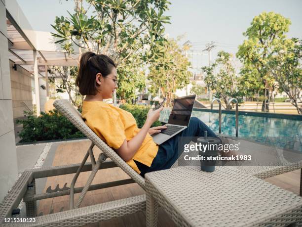 junge frau arbeitet auf ihrem computer im urlaub in der nähe von pool. - itinerant stock-fotos und bilder
