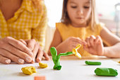 Young mother and her junior daughter playing with plasticine