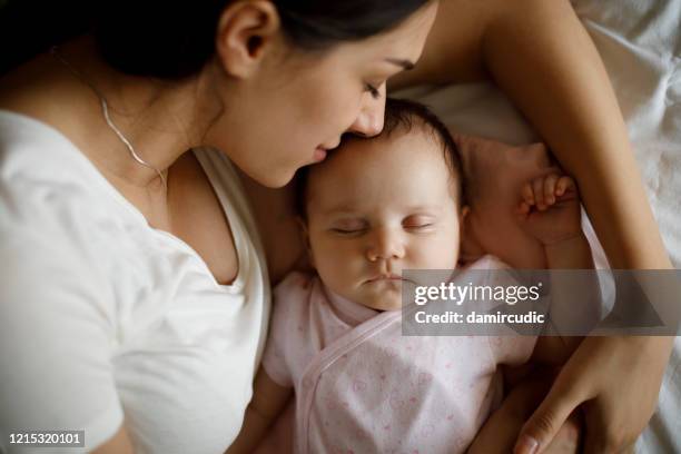 hermosa joven madre y su lindo bebé durmiendo en la cama en casa - baby and mom fotografías e imágenes de stock