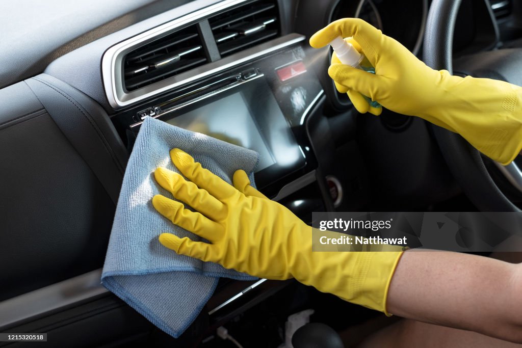 Wiping down surface of car dashboard with 70% alcohol spray and disposable damp cloth