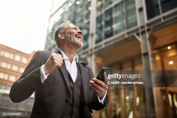 ecstatic businessman learning good news on smart phone - mobile phone reading low angle stock pictures, royalty-free photos & images