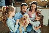 Happy parents and their daughters having fun with a dog at home.