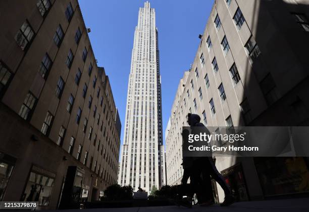 People walk along 5th Avenue in the empty plaza in front of 30 Rockefeller Center as coronavirus stay at home orders have kept most people off the...