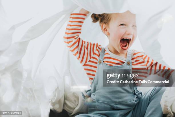 playful girl under a white sheet - bedclothes stock-fotos und bilder