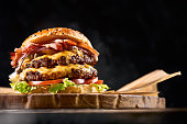 Juicy burger on the board, black background. Dark background, fast food. Traditional american food. Copy space