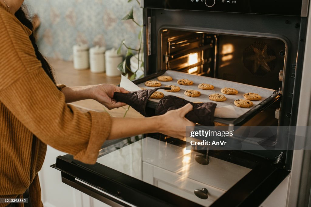 Jonge moeder die een dienblad hoogtepunt van koekjes in de oven zet