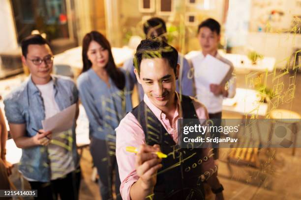 ung asiatisk affärsman som drar på transparent wipe board framför sitt multietniska team - genomskinlig skrivtavla bildbanksfoton och bilder