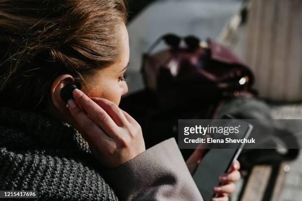 person with mobile phone and bluetooth headset, typing on telephone in the street - in ear headphones stock-fotos und bilder