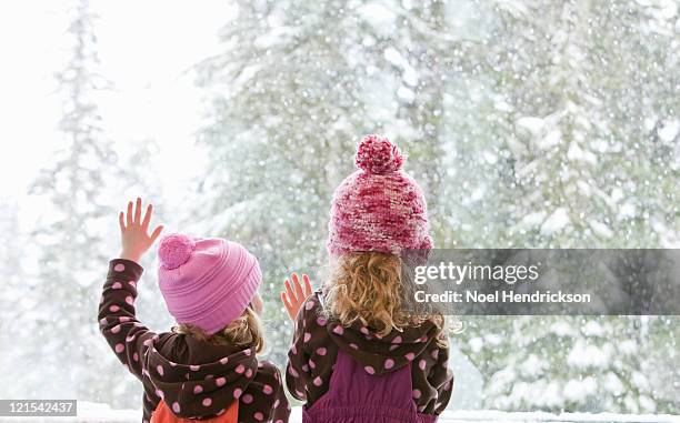 young sisters look at snowfall outside - frost scheibe stock-fotos und bilder