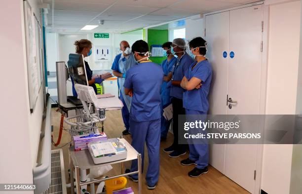 Members of medical staff wearing PPE , including face masks, aprons and gloves as a precautionary measure against COVID-19, gather in a corridor for...