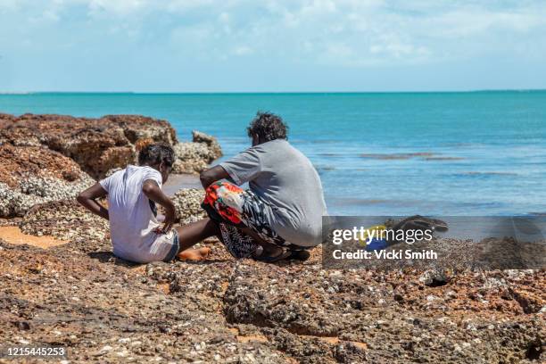 young indigenous teenager and mother woman on the rocks overlooking clear blue ocean waters - australian aboriginal culture stock pictures, royalty-free photos & images