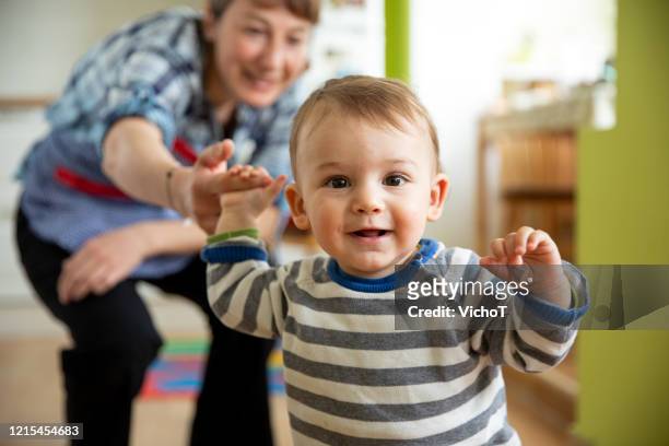 young mother supporting her son with his first attempts to walk - childhood development stock pictures, royalty-free photos & images