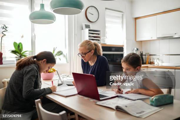 homeschooling - madre che aiuta le sue figlie a finire i compiti scolastici durante la quarantena del coronavirus - lavoro a domicilio foto e immagini stock