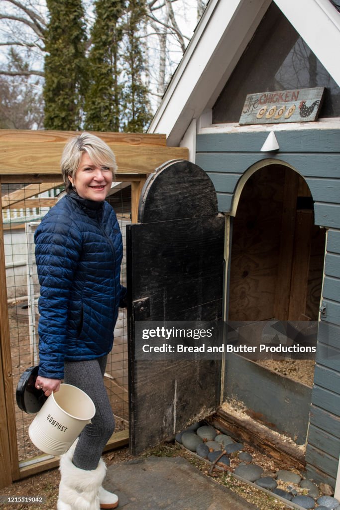 Smiling woman standing at door to chicken coop holding compost pail