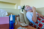 Woman lying covered with blanket using vapor steam inhaler nebulizer mask inhalation at home on the bed medicament treatment asthma pneumonia bronchitis coughing sick