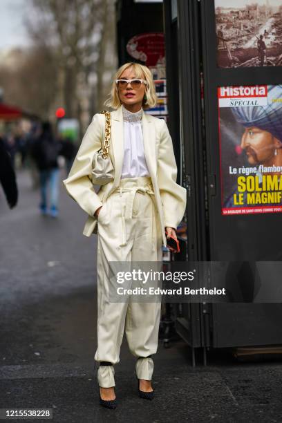 Viktoria Rader wears sunglasses, a cream-color pale yellow silky lustrous blazer jacket, a Bottega Veneta puff bag with a golden chain, a white...
