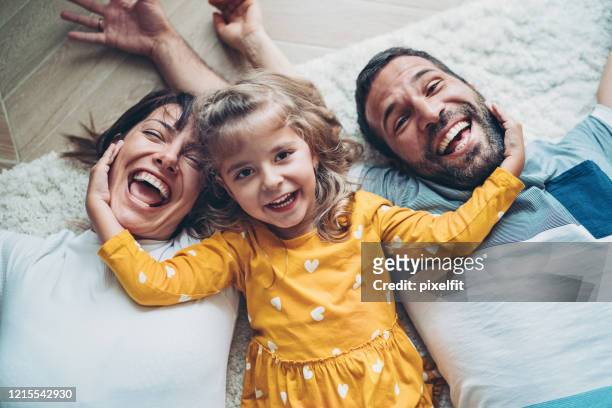 lycklig familj med en liten flicka som ligger på golvet - couple laughing hugging bildbanksfoton och bilder