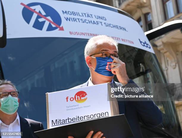 May 2020, Hessen, Wiesbaden: Tarek Al-Wazir , Minister of Economics of the State of Hesse, stands in front of a coach with the inscription "Sichern...