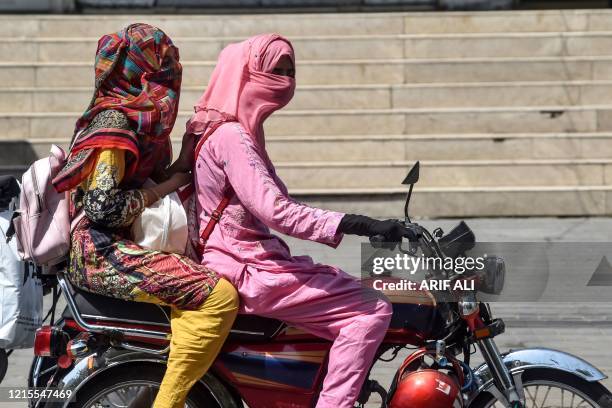 Women covering their faces ride a motorbike on a street during heatwave, as temperatures reach 40 degrees celsius, in Lahore on May 27, 2020.