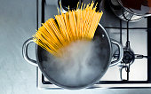 Cooking raw spaghetti in the boiling water contained in a saucepan