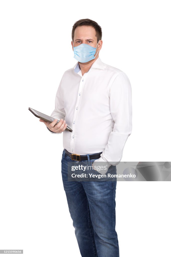 Man with digital tablet in white shirt and jeans wears surgical mask to protect from virus. Isolated on white background