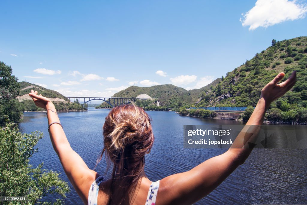 A Woman Raising Arms In Happiness Against Beautiful Lake