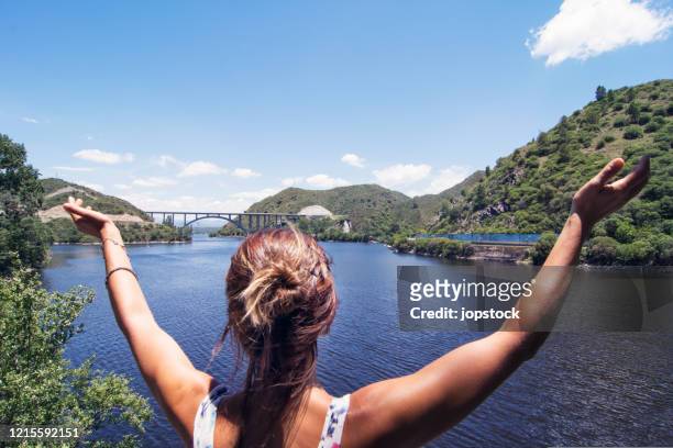 a woman raising arms in happiness against beautiful lake - cordoba argentina stock-fotos und bilder