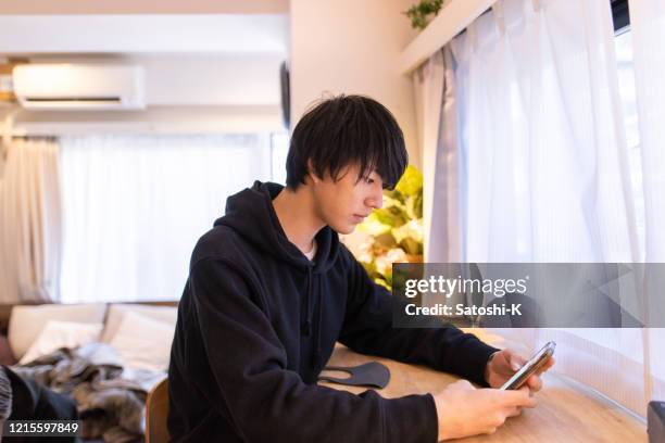 部屋でスマートフォンを使う若い男 - 美大生　日本 ストックフォトと画像