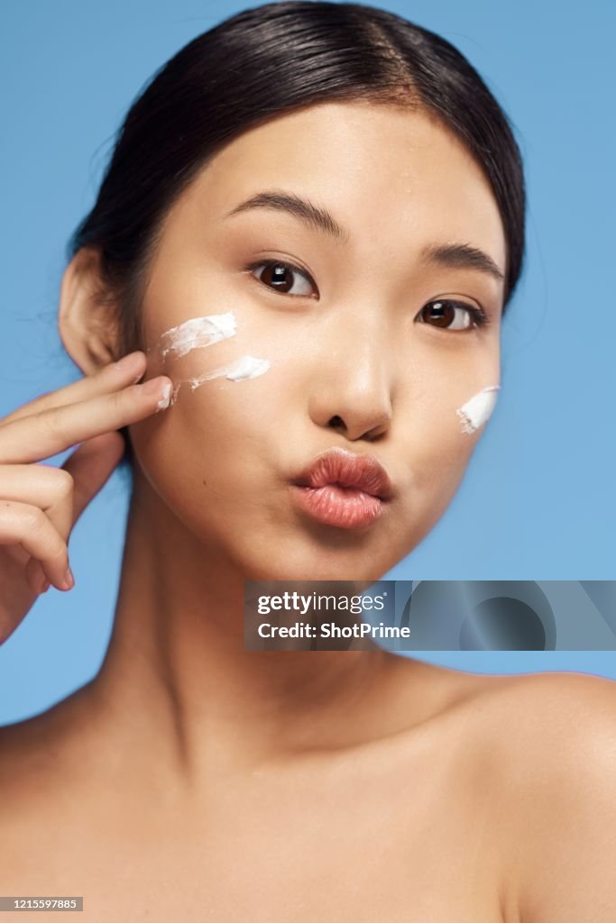 Beauty portrait of a young Asian woman with clean and healthy skin who applies cream to her face.