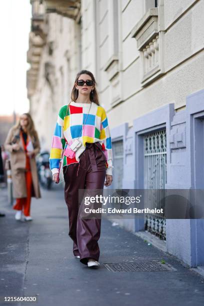 Natalia Ostrofsky wears earrings, sunglasses, a colorful patchwork knit top, dark brown leather wide-legs full-length pants, white shoes, a Fendi...