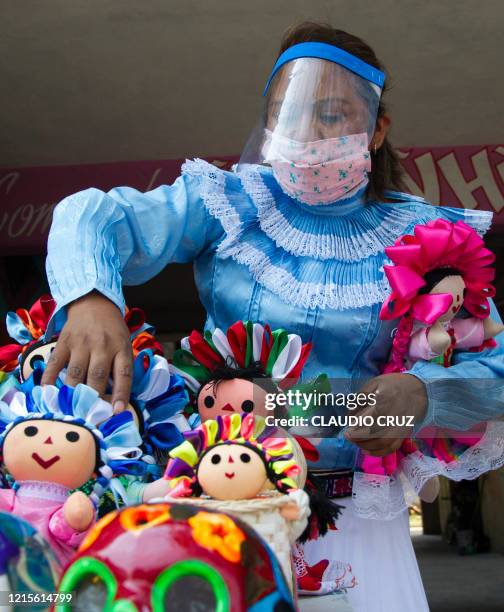 Mariana Gonzalez of the indigenous Otomi ethnic group arranges her craft dolls wearing a face shield as a preventive measure against the spread of...