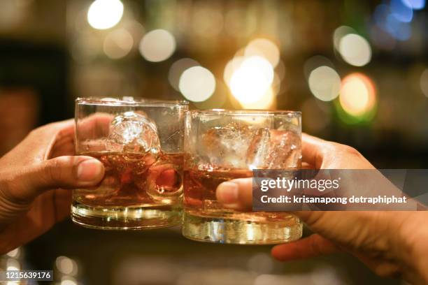 two men clinking glasses of whiskey drink alcohol beverage together at counter in the pub - cognac stockfoto's en -beelden