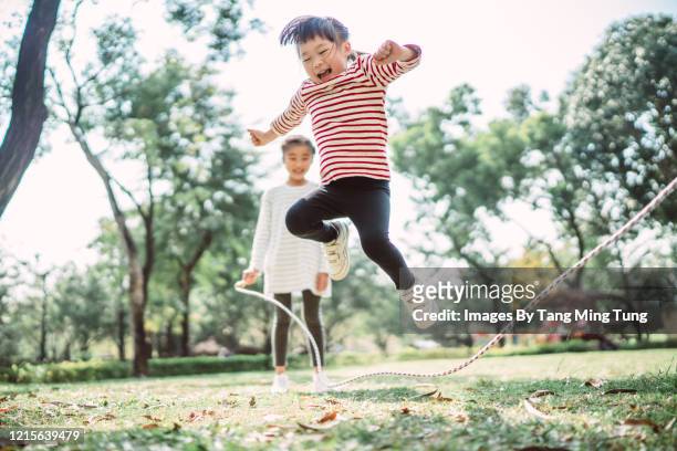 young family jumping rope joyfully on the lawn - 4 people playing games stock-fotos und bilder