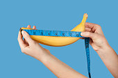 Measuring the size of a banana as a symbol of the male penis isolated on blue background. Big dick length. Strong erection and impotence problem