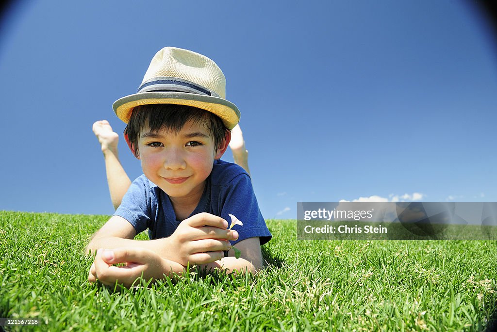 Boy laying in the grass wearing a straw hat