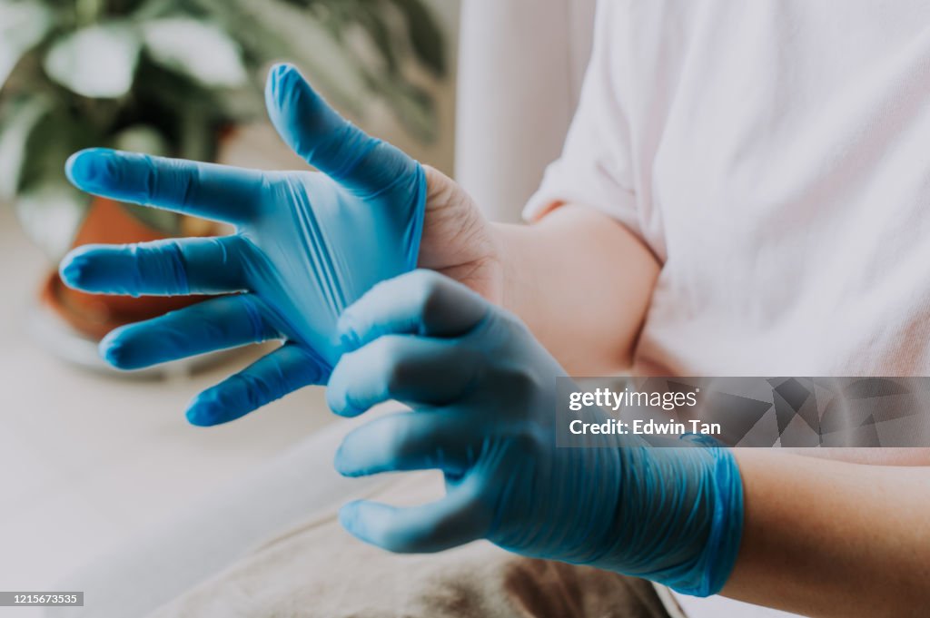 Eine asiatische Chinesin, die ihre Latex-OP-Handschuhe zu Hause vor dem Reinigungsprozess trägt